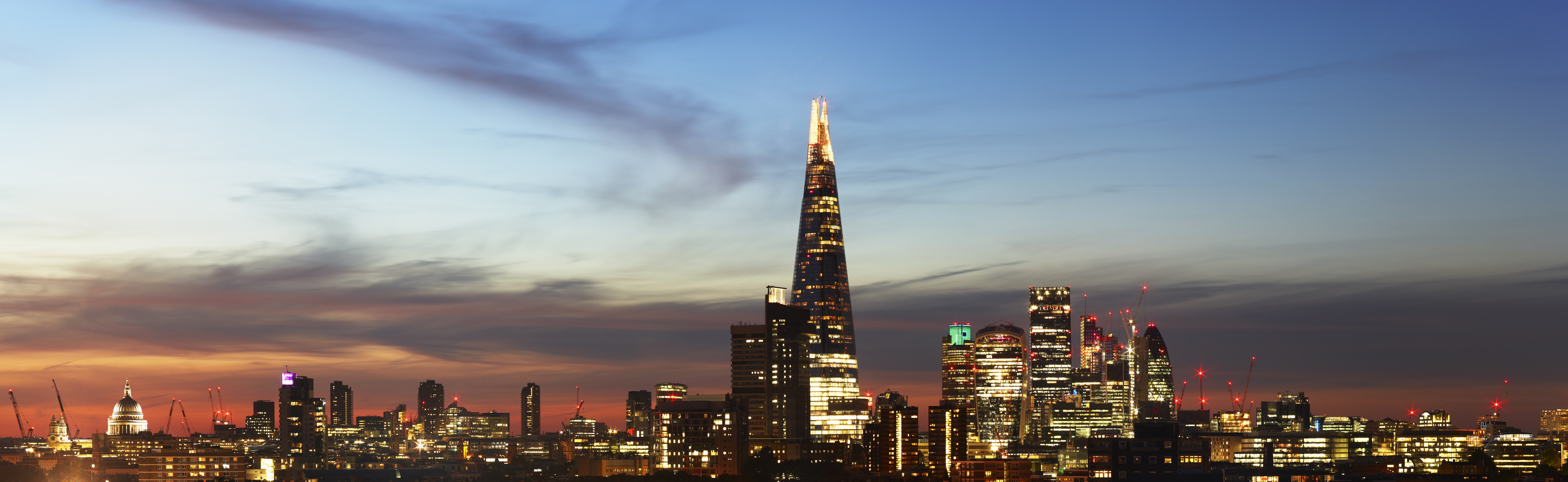 A landscape view of London city at dusk with well-lit buildings making up a skyline